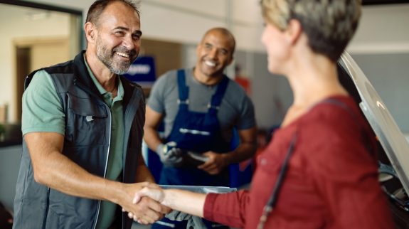 Happy car mechanic and his customer shaking hands while greeting in auto repair shop.